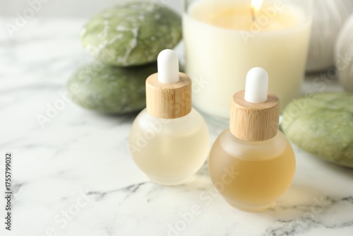 Beautiful spa composition with essential oils and burning candle on white marble table, closeup. Space for text