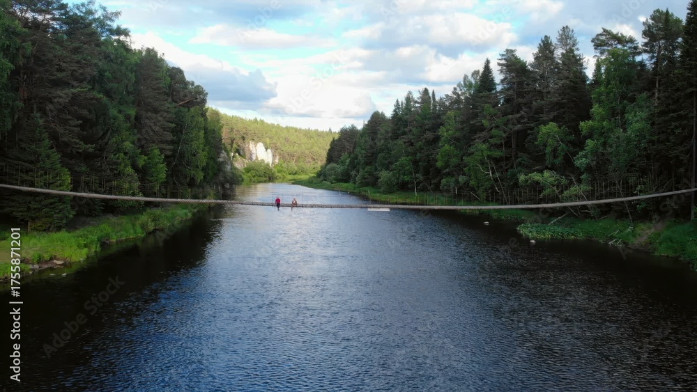 Fototapeta premium Tourists relaxing on rope bridge over scenic river