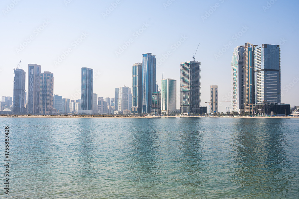Fototapeta premium Modern skyscrapers along turquoise waterfront in sunny day, urban coastal view. 