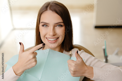 Bild auf Leinwand Smiling beautiful girl is sitting in dentistry chair with positive emotion and gesturing fingers up
