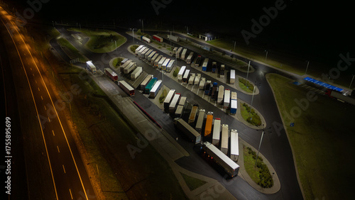 Aerial view of a truck stop at night, showcasing rows of parked semi-trucks illuminated by streetlights.
