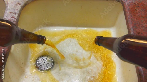 A man pours 2 bottles of spoiled waste cider or beer to the sink