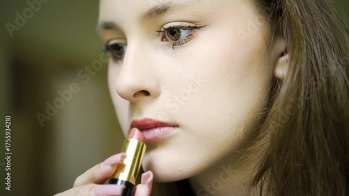 Close-up of a beautiful teenage girl applying lipstick on her own. Young, stylish and well-groomed, practicing makeup independently. Focus on lips and cosmetic process in natural light.