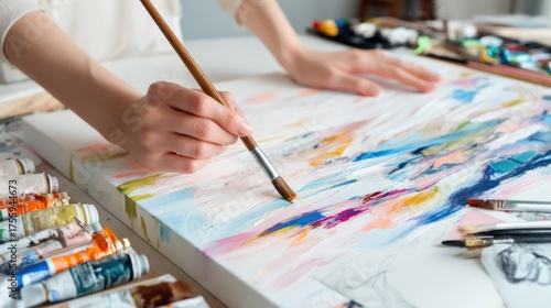 Hands painting abstract brush strokes on a canvas for DIY wall art, surrounded by paint supplies and inspiration sketches