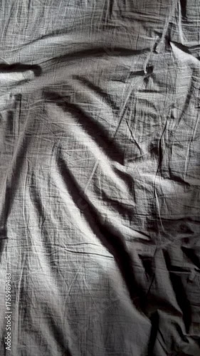 a wrinkled gray bed sheet with a ray of sunlight woman hand