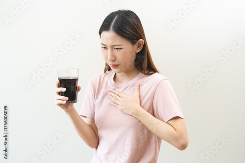 Acid reflux disease, suffer asian young woman, girl hand holding a glass of cola, have symptom gastroesophageal, heartburn pain on chest when drinking sparkling, soft water. Healthcare medical concept