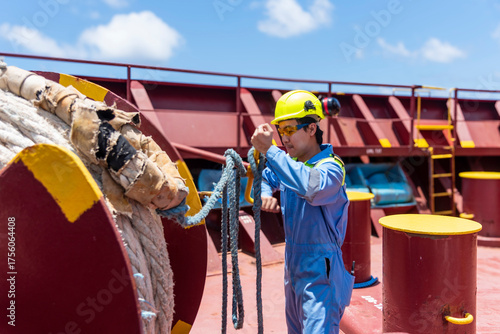 Young male officer in blue coveralls and yellow safety helmet operating a mooring winch on board of merchant ship.