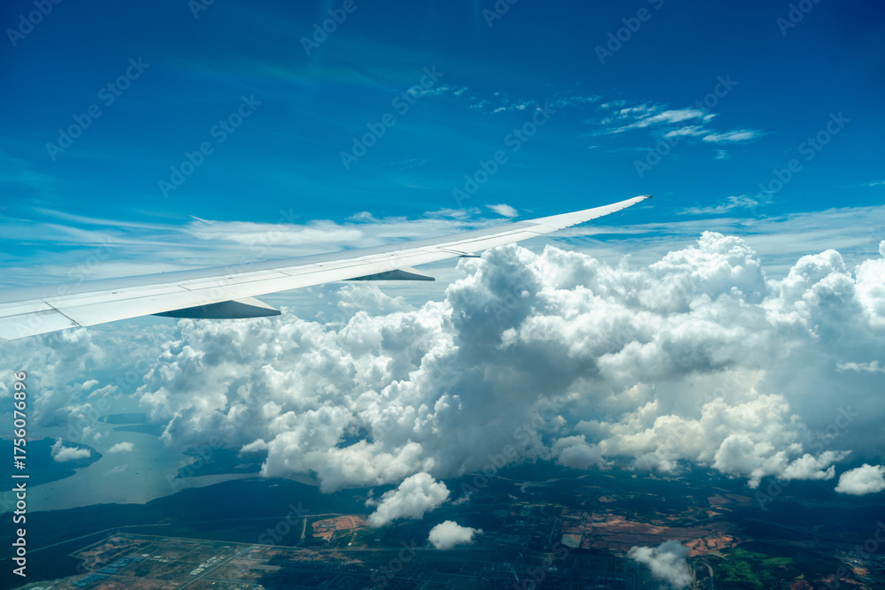 Obraz premium Airplane wing above coastline and clouds in bright sky