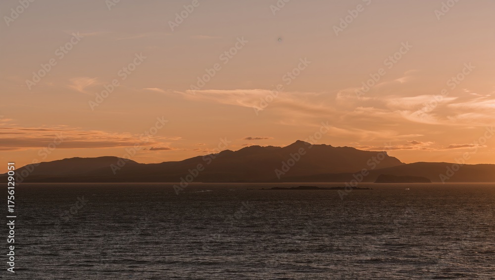 Naklejka premium Stunning mountain outline against a sunset over the ocean with charming clouds