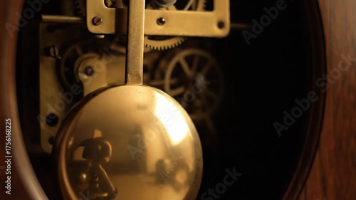 Close up of a pendulum clock mechanism with gears and a golden weight