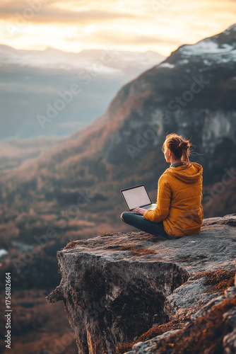 Woman working on laptop outdoors on mountain edge, scenic landscape behind