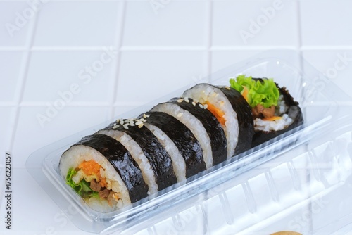 Close up of fresh Korean gimbap roll with vegetables in plastic container, traditional Asian snack food.