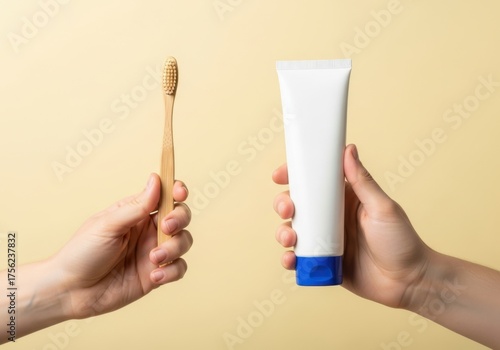 Hands holding a bamboo toothbrush and a tube of toothpaste on a beige background, promoting sustainable oral hygiene practices for a healthy smile