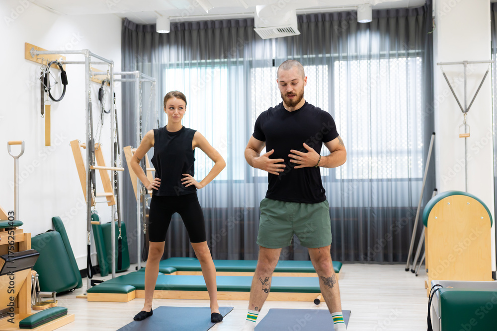Fototapeta premium stretching, couple doing Pilates exercises. exercises to strengthen body and stretch. practicing physical fitness exercises on Pilates machine. Reformer pilates studio machine for fitness workouts 