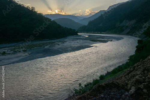Teesta river flowing through Himalayan mountains, sunlight coming through clouds in the background, setting sun behind mountain peaks. Sikkim, India.
