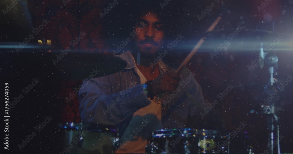 Fototapeta premium Playing drummer wearing light denim shirt over white T-shirt in dimly lit stage, with drum kit