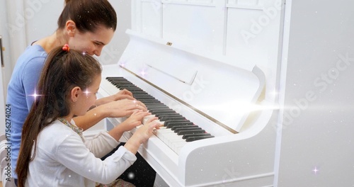 Sitting mother and daughter pressing keys on white upright piano at home, with bench and sparkles