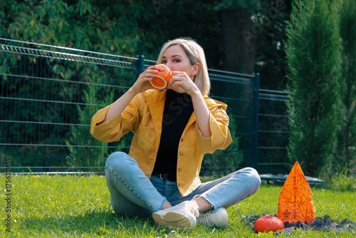 A beautiful girl is sitting on the terrace on a sunny day, drinking from a Halloween mug 