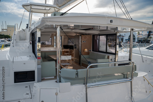 Contemporary catamaran exterior and interior with an open living space featuring light green cushioned seating, dining area, and modern kitchen. Polished chrome supports and large windows enhance the