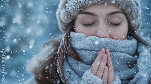 Winter portrait of woman with closed eyes in snow wearing warm scarf and hat