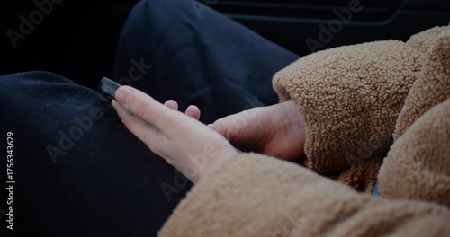 Close-up of a person in a fleece jacket holding a smartphone while seated in a car. The screen displays an incoming call interface, highlighting relaxed communication, technology, and travel.