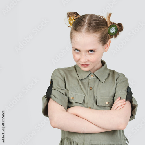 Fotografija Smirking caucasian young girl with fruit hair accessories in green outfit, arms crossed, confident expression