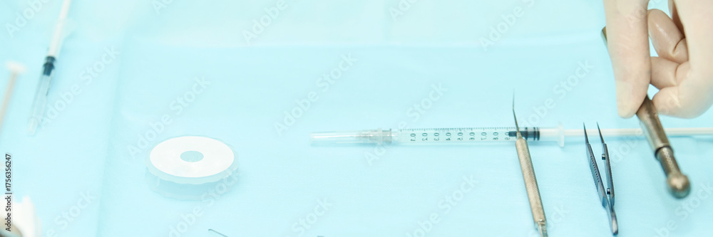 Naklejka premium Surgical tools and medical equipment on blue surface with gloved hand preparing instruments.