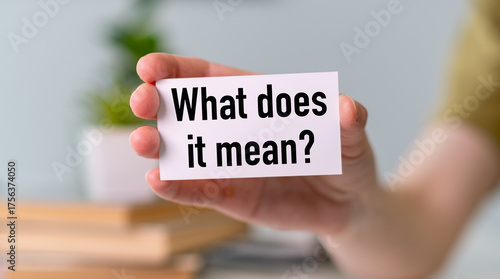 A person is holding a white card that says What Does it Mean. Concept of curiosity and contemplation, as the person is holding the card and pondering its meaning