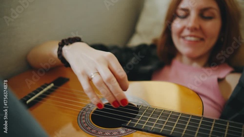 Woman enjoying playing guitar while sitting comfortably on a couch in a cozy indoor setting during a relaxed afternoon