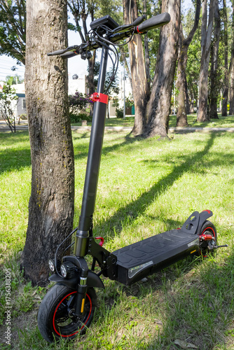 Electric scooter parked near tree in sunlit grassy park setting, electric scooter concept