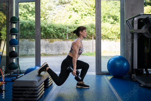 Woman exercising with dumbbells, bulgarian split squat, showing resilience
