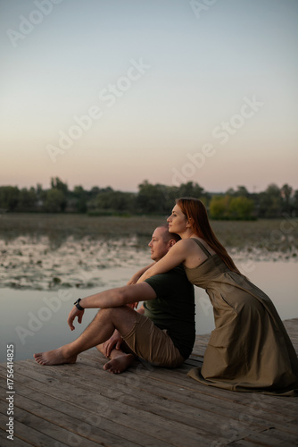 A woman hugs a man from behind and looks into the distance at the water at sunset