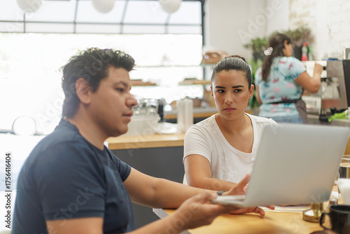 Jóvenes profesionales latinos discuten ideas y colaboran en un proyecto usando una laptop en un moderno café.