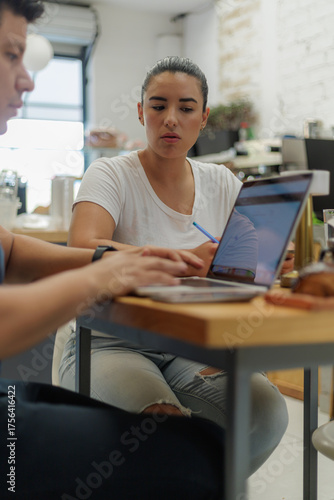 Joven pareja de negocios colaborando en un portátil en un café moderno, discutiendo ideas y trabajando en un proyecto.