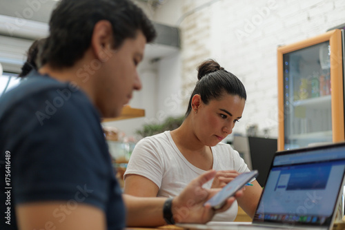 Joven mujer hispana concentrada trabajando en laptop y teléfono con colega en primer plano