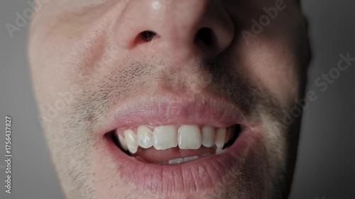Extreme macro shot of the lower part of a man's face. Lips pull back to reveal white teeth in a grimace with unshaven stubble and detailed skin texture visible around the tense mouth area.