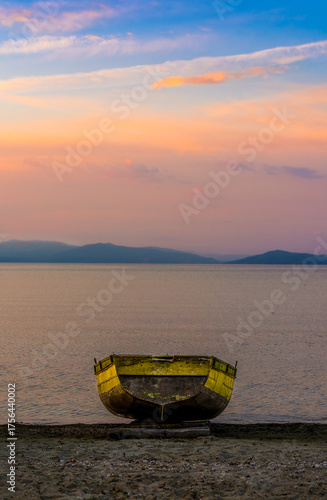 Old wooden boat resting on the shore at sunset with colorful sky reflections over Lake Ohrid and distant mountain silhouettes