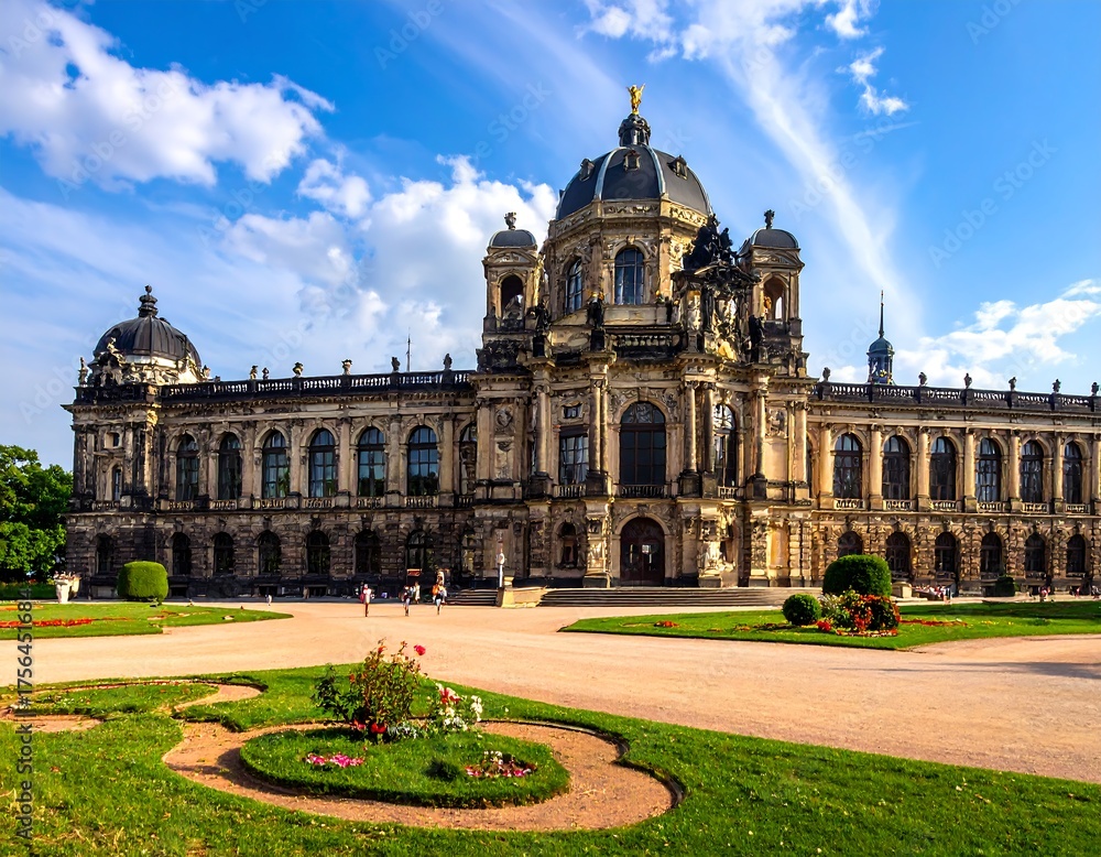 Fototapeta premium A stunning baroque palace with ornate details sits under a bright blue sky, surrounded by manicured gardens and lush greenery