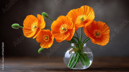Vibrant bouquet of freshly picked orange poppy flowers with green stems arranged in round glass vase on wooden surface