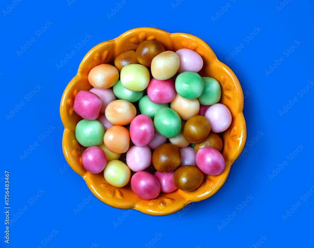 Obraz premium Flat lay of colourful candy in orange bowl isolated on blue background