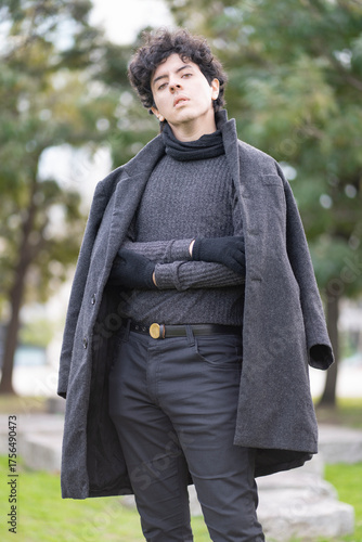 Stylish young man with curly hair posing dramatically in a long coat