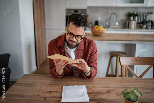 Fotografie Man opening and reading paper mail at home kitchen table