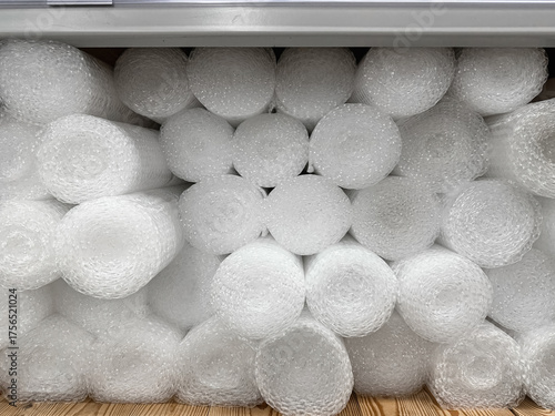A close-up of stacked white bubble wrap rolls in a metal industrial shelf, providing essential cushioning for fragile items in shipping, storage, and packaging applications.