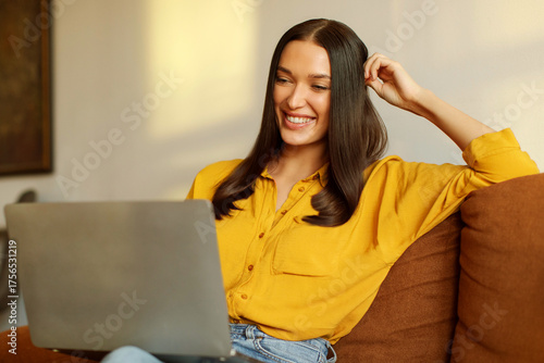 Canvas Print Smiling lady freelancer working from home, sitting on couch and using laptop, su