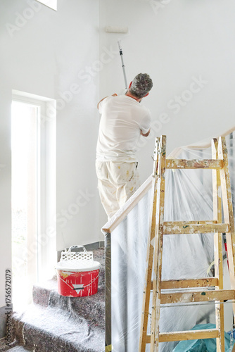 Painter on ladder applying primer to wall