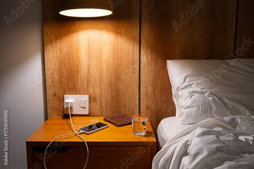 Mobile phone charging on bedside table in comfortable hotel or home bedroom.