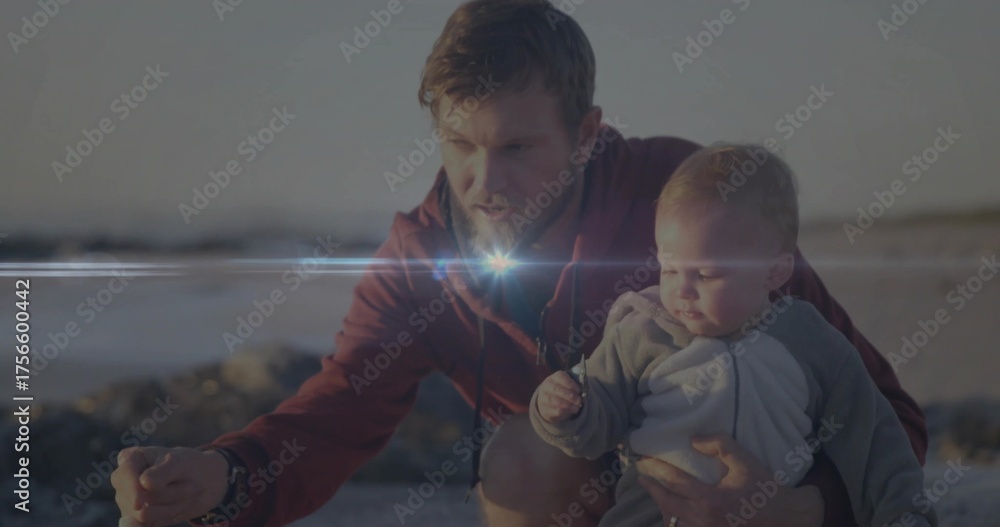 Naklejka premium Crouching father holding baby boy pointing toward wet sand on beach in afternoon, with small shell