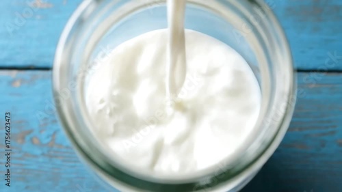 Pouring Milk into a Glass Jar on Blue Wooden Surface.