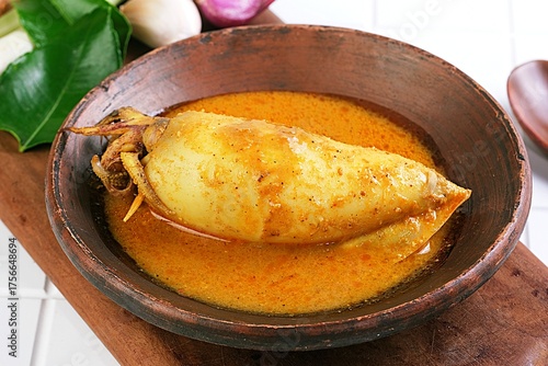 Close-up of gulai cumi, Indonesian squid curry with coconut milk, served in wooden bowl with spices.