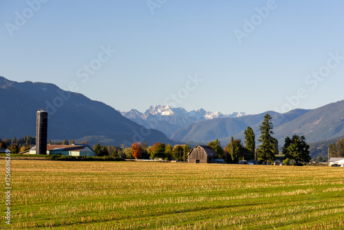 Farmland with harvested fields, barn, and silo set against the majestic Cascade Mountains in British Columbia, Canada